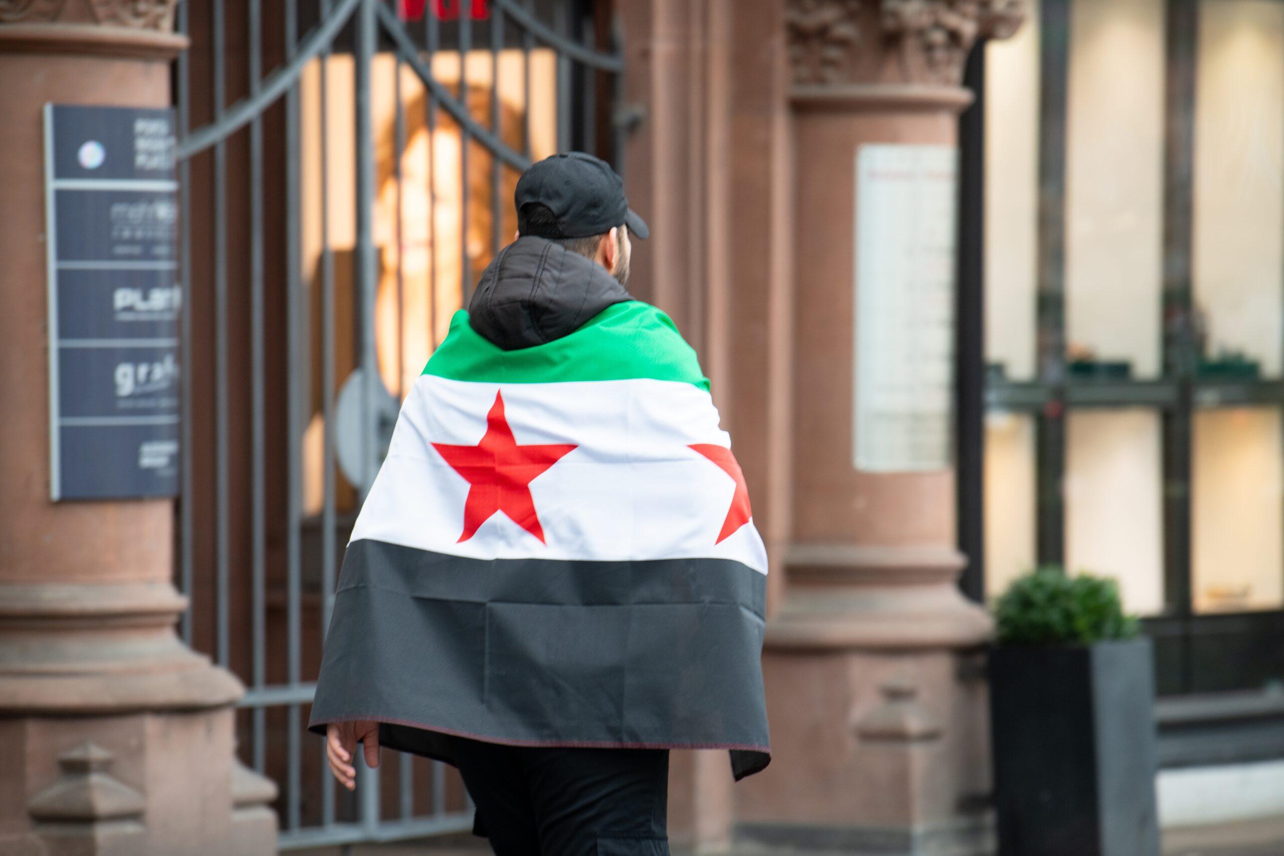 شخص يضع على كتفيه علم الثورة السورية، كما في صورة المقال الأصلي